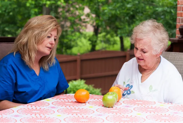 Two women sitting at a table with an orange and apple.