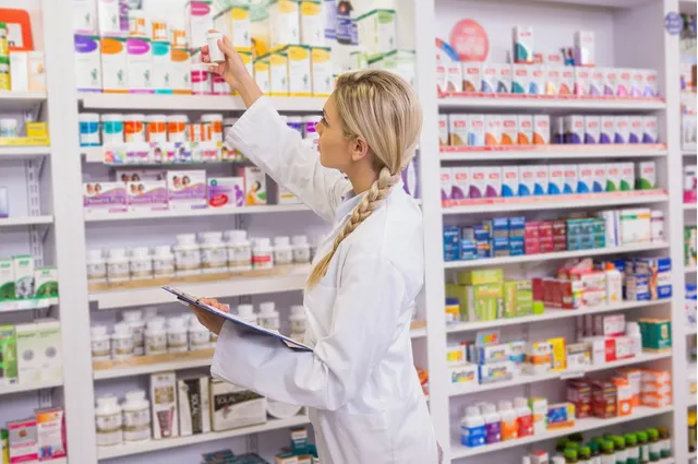 A woman in white lab coat looking at medicine on shelves.